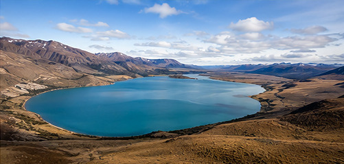Aerial view of a deep blue lake surrounded by arid Patagonian hills